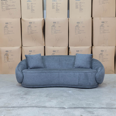 The Noosa Curved Fabric Three Seat Sofa - Dark Grey available to purchase from Warehouse Furniture Clearance at our next sale event.