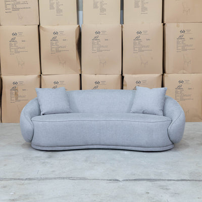 The Noosa Curved Fabric Three Seat Sofa - Light Grey available to purchase from Warehouse Furniture Clearance at our next sale event.
