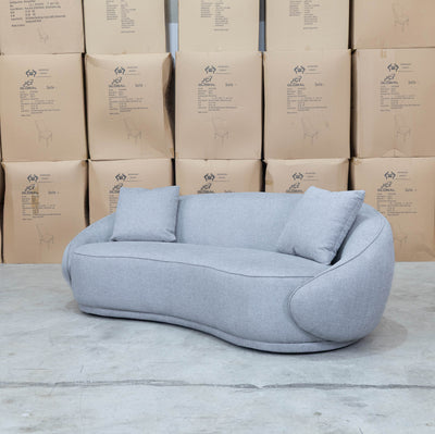 The Noosa Curved Fabric Three Seat Sofa - Light Grey available to purchase from Warehouse Furniture Clearance at our next sale event.